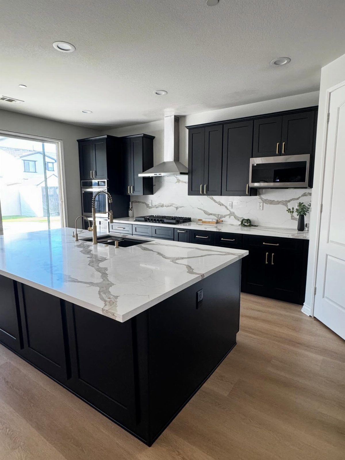 Black kitchen cabinets with white marble countertops and light wood floors.