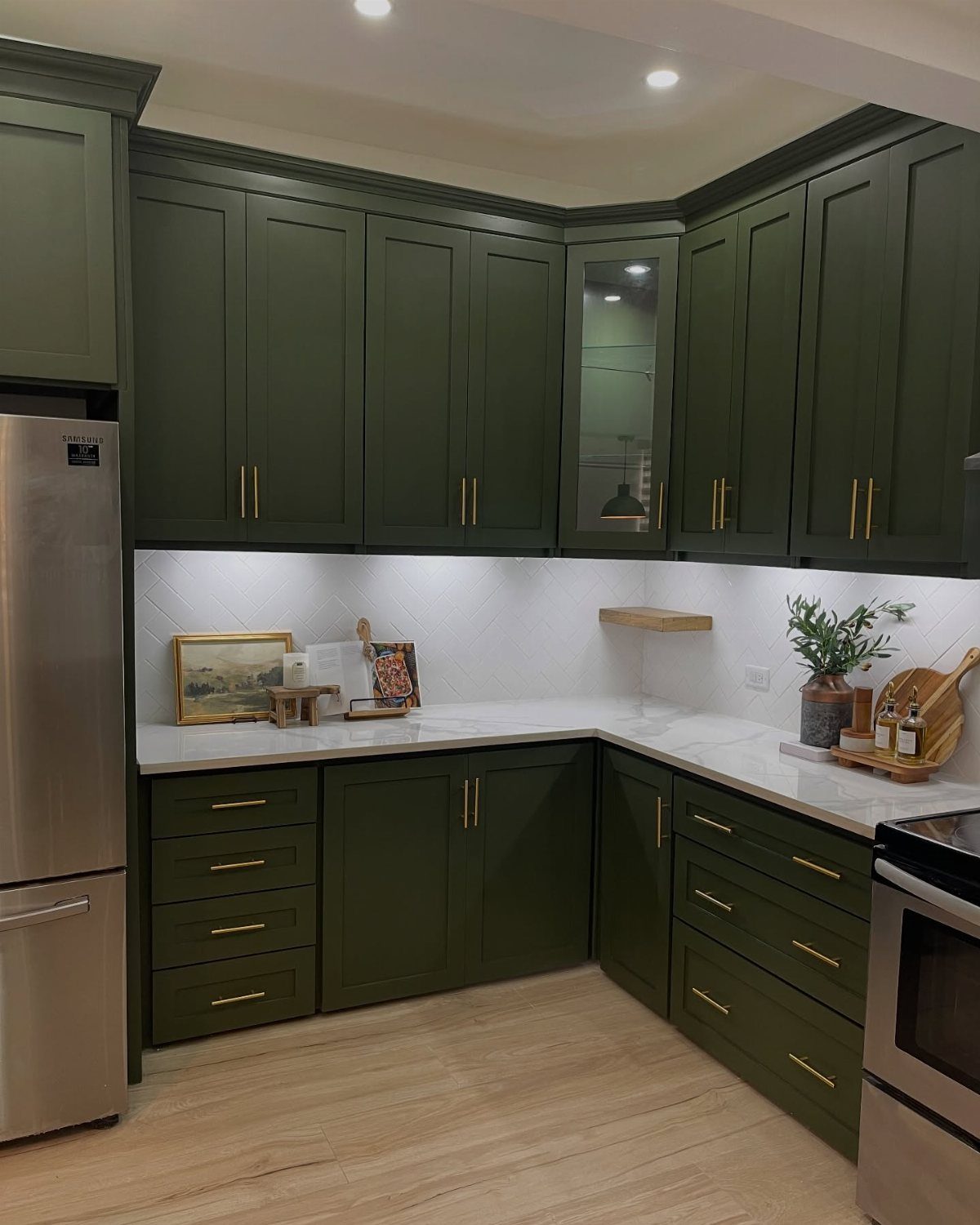 Sage green kitchen cabinets with gold hardware and white countertops in a modern kitchen.