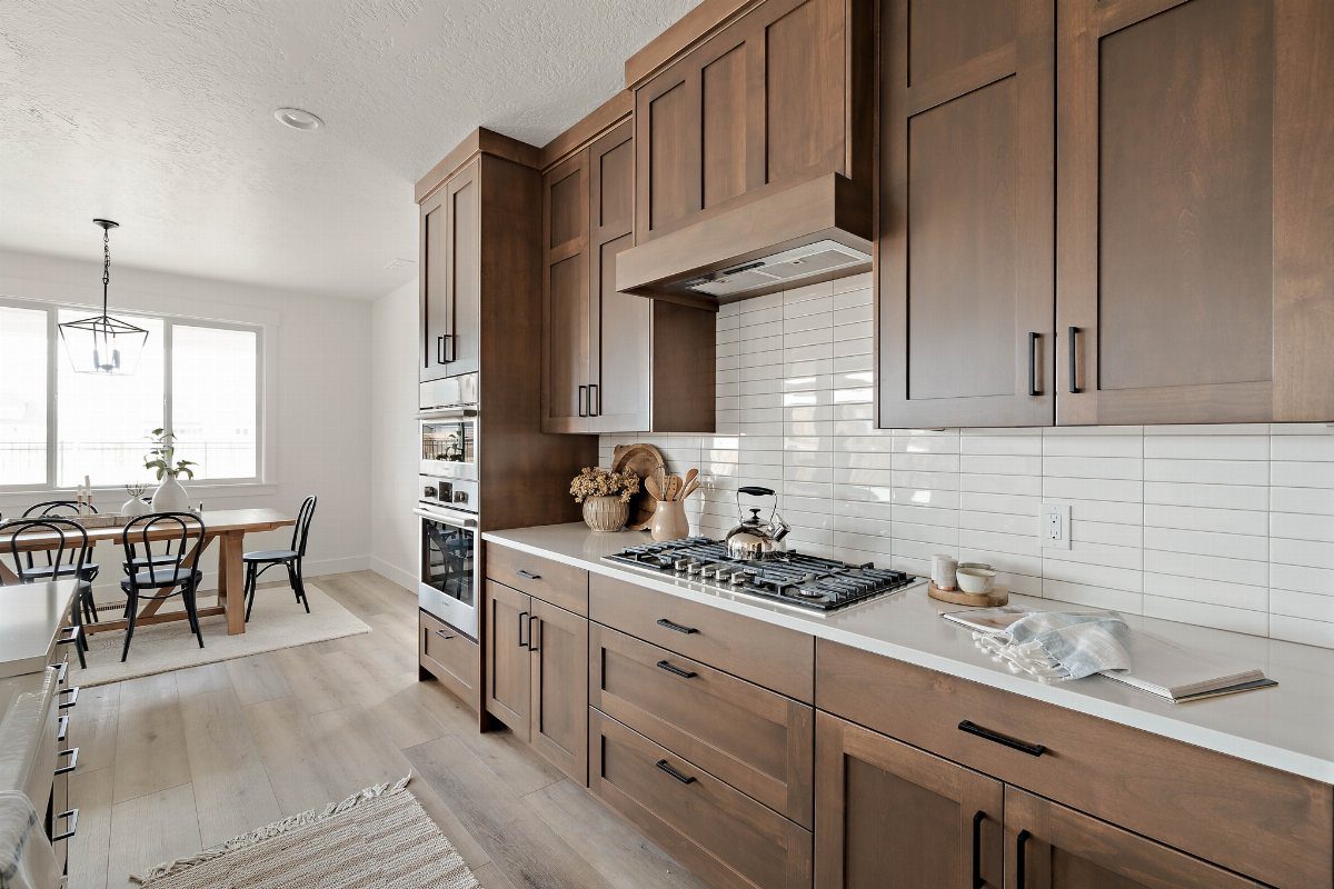 Medium-brown stained wood kitchen cabinets with white countertops and a tiled backsplash.