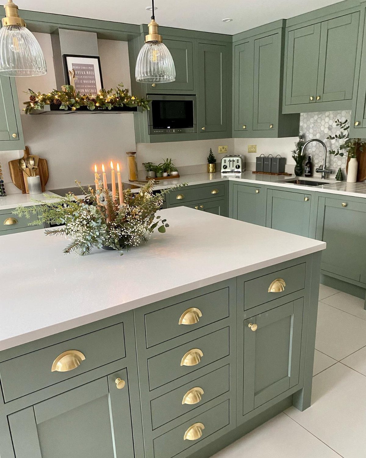 Sage green kitchen cabinets and island with white countertops and gold hardware accents.