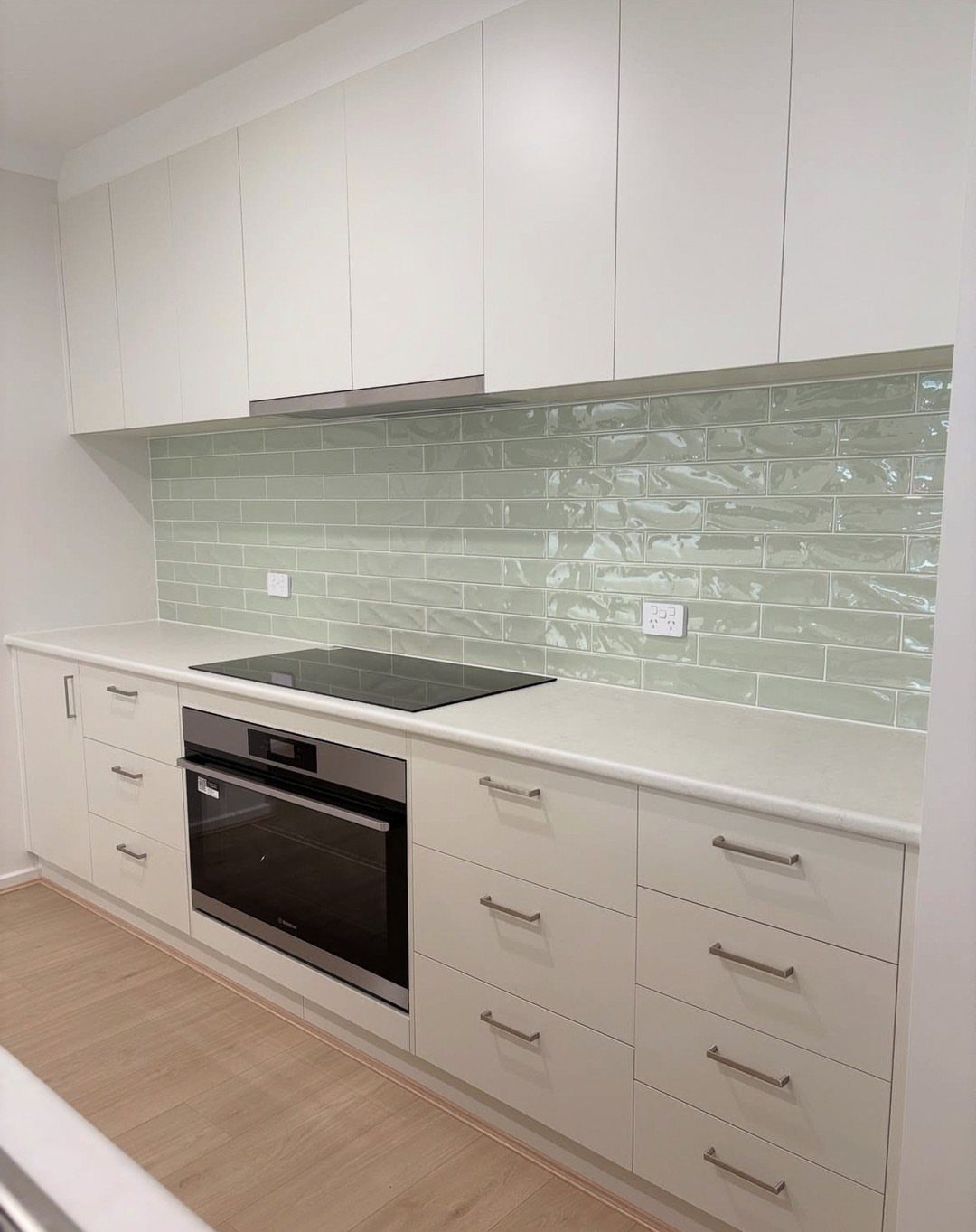 Sage green subway tile backsplash between white kitchen cabinets and white countertops.