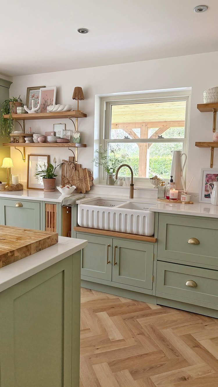 Sage green kitchen cabinets with a white farmhouse sink and herringbone wood floors.