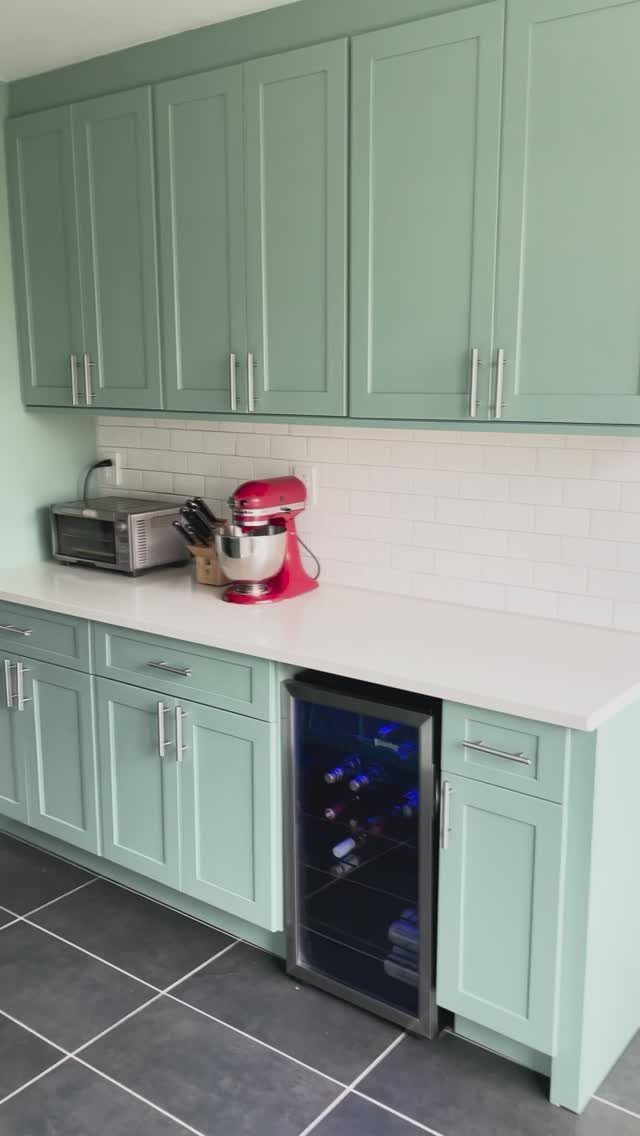 Sage green shaker cabinets with white countertops and a red stand mixer.