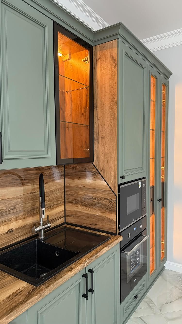 Sage green kitchen cabinets with wood grain countertops and a matching wood backsplash.