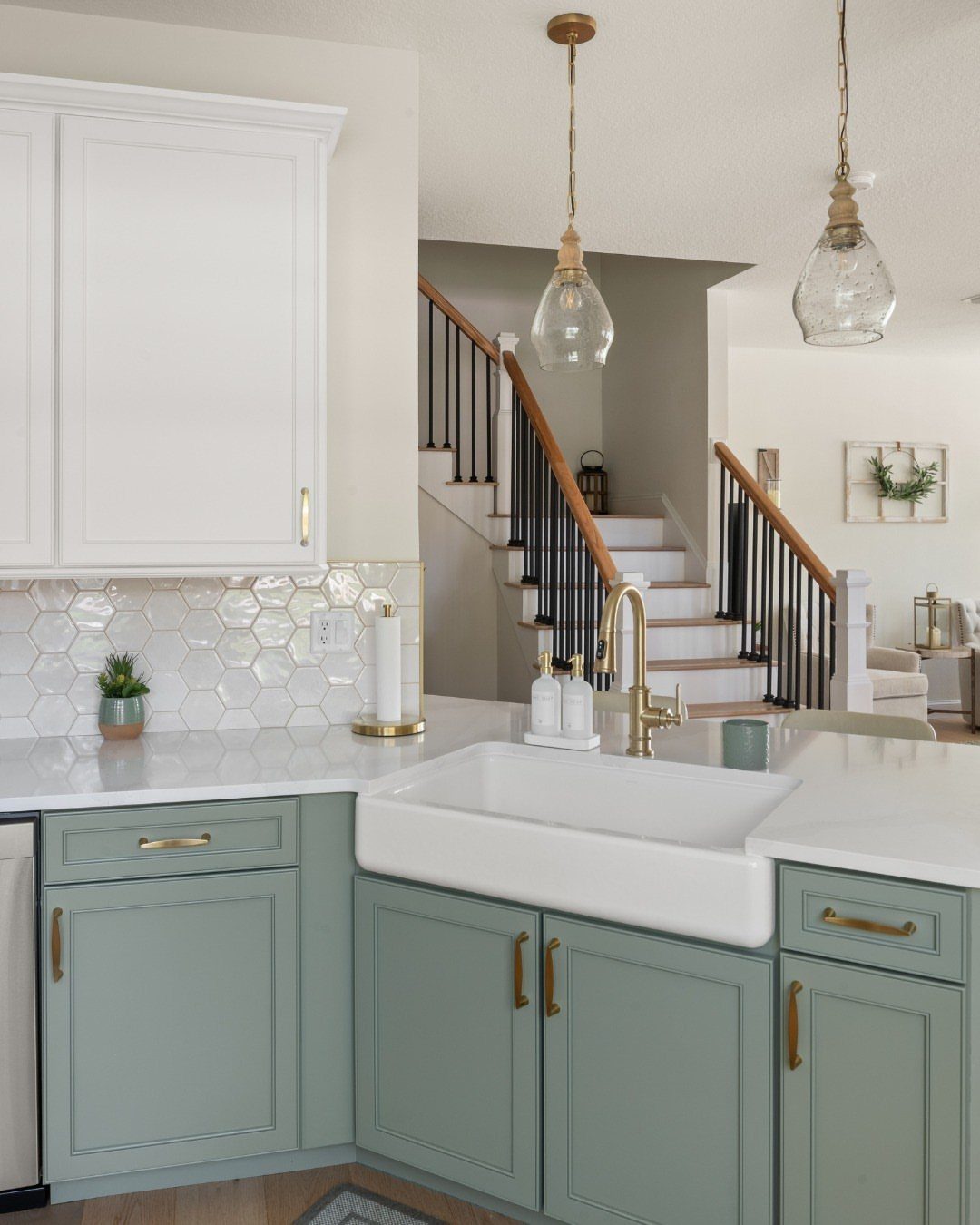 Sage green lower cabinets and white upper cabinets with gold hardware and farmhouse sink.