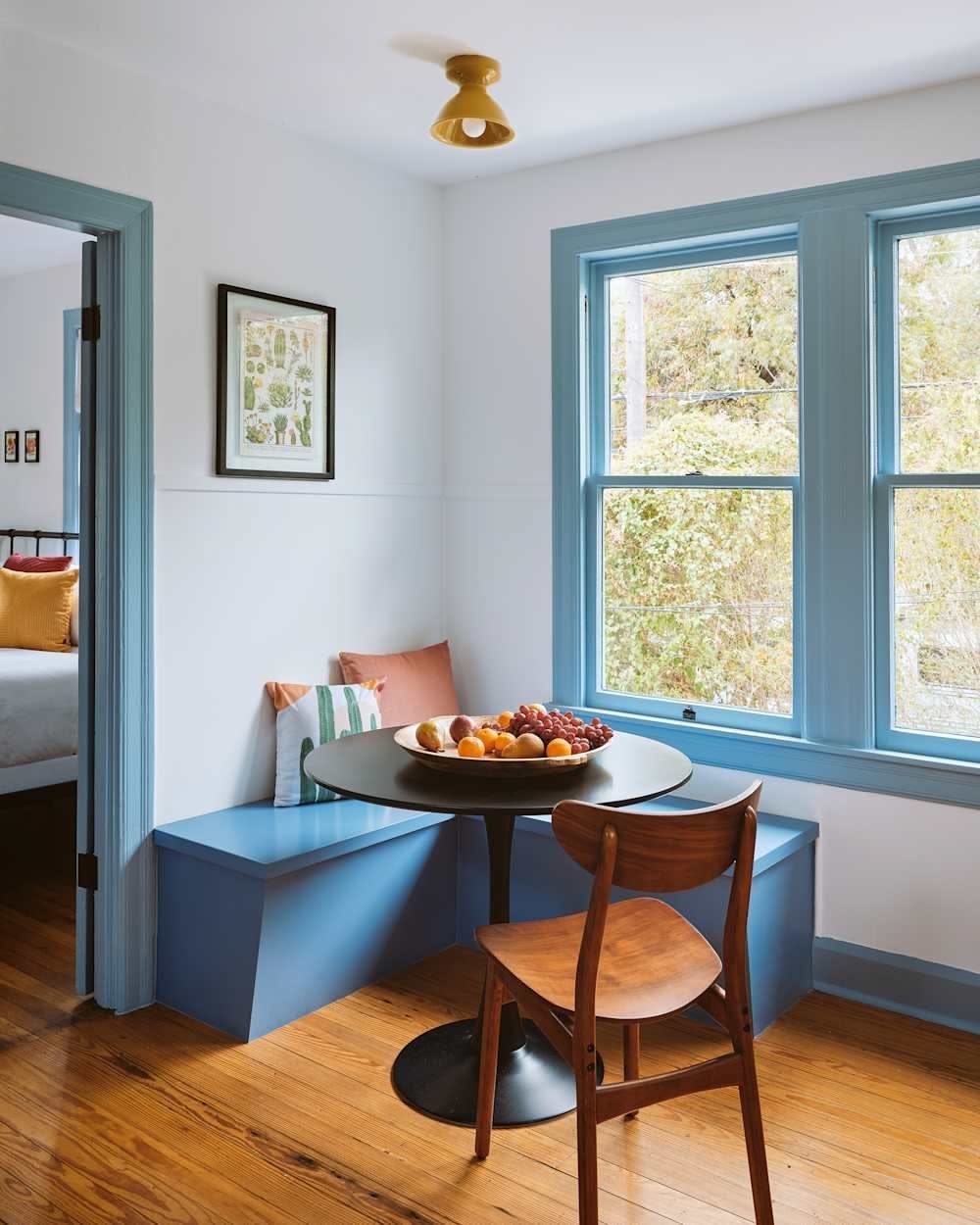 Round black dining table with blue L-shaped built-in bench seating by a window.
