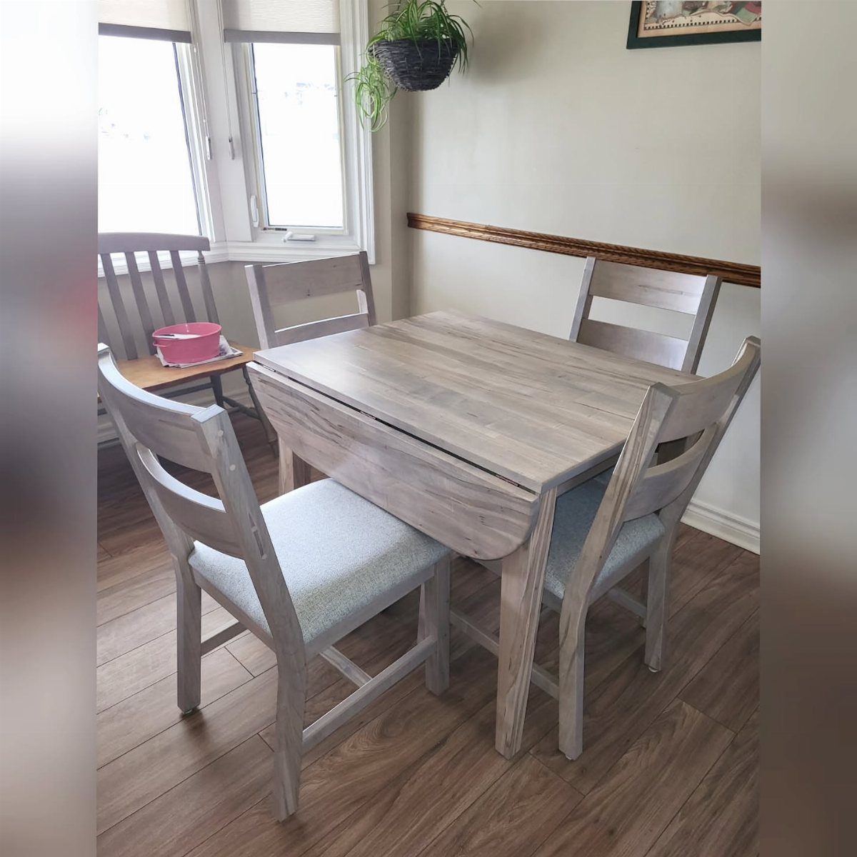 Light grey wood drop leaf dining table with four matching upholstered chairs.