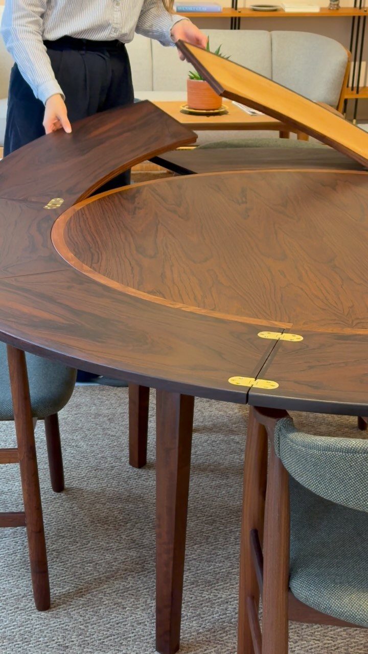 Round walnut extendable dining table with leaves being lifted by a person