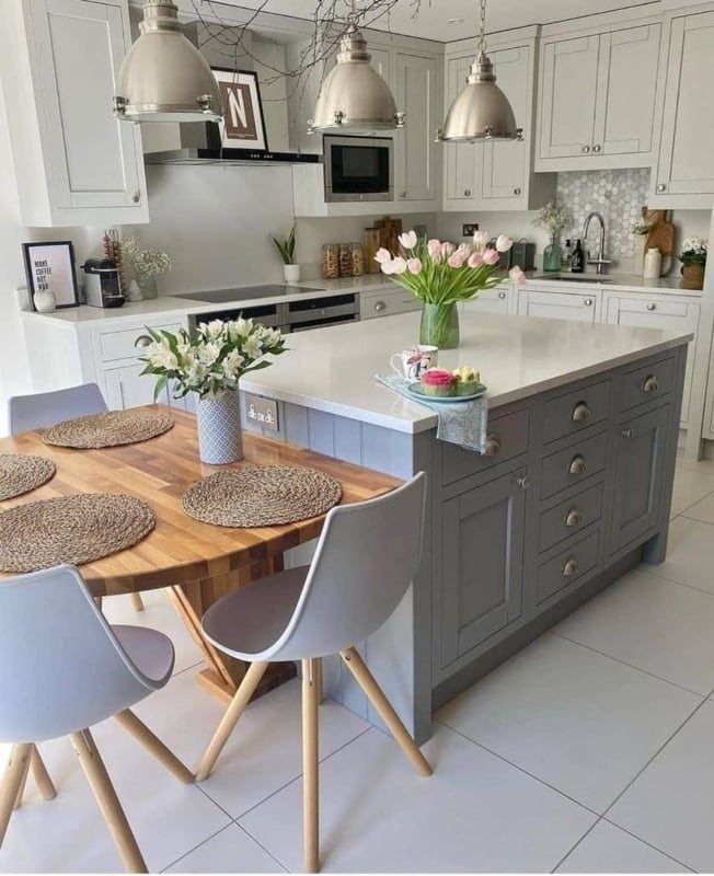 Wooden dining table integrated into a grey kitchen island with modern grey chairs.