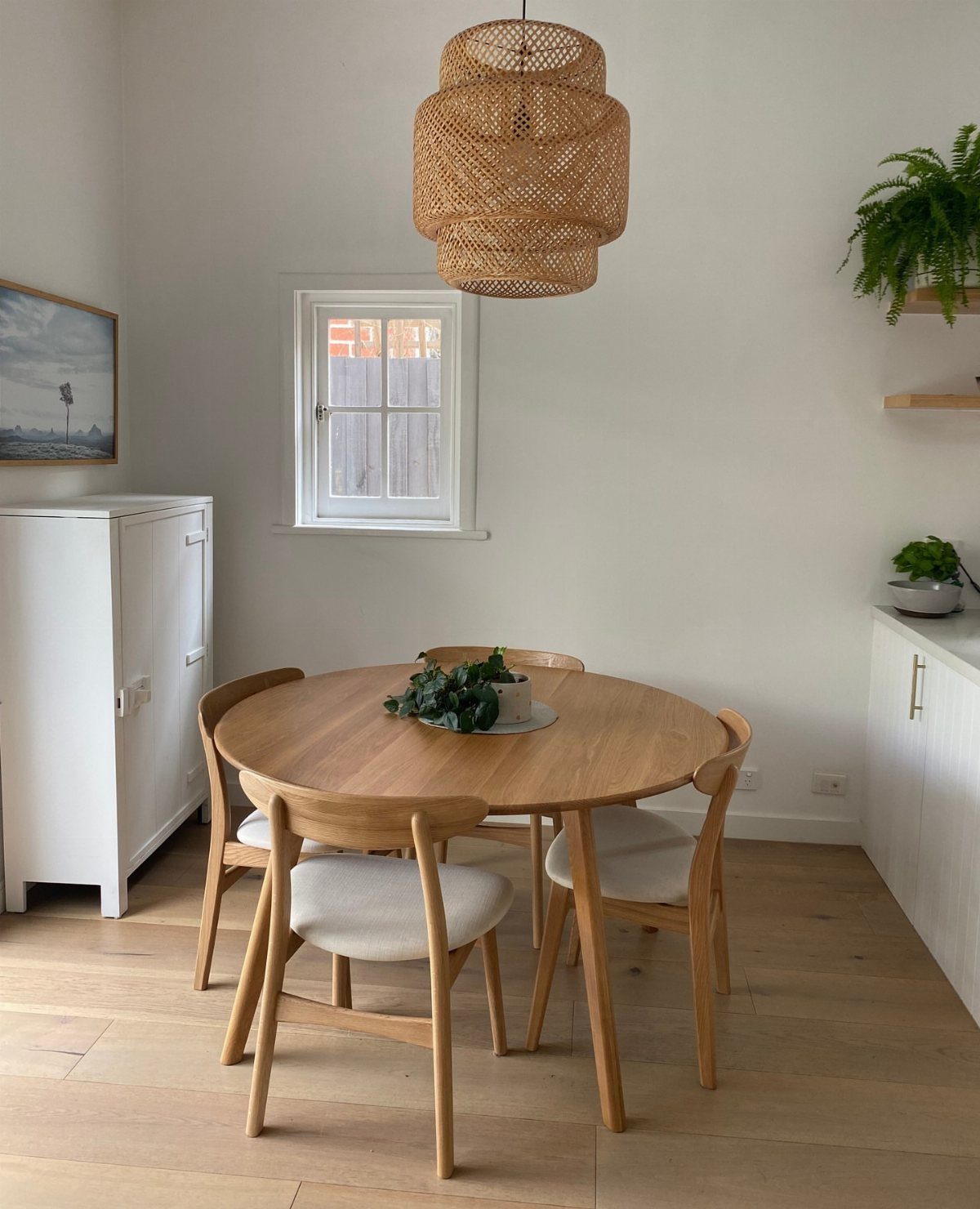 Round wooden dining table with four chairs and a wicker pendant light.