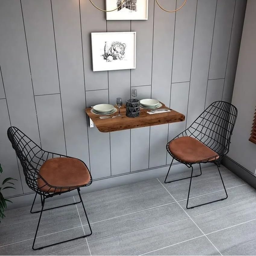 Wall-mounted wooden dining table with two black wire chairs against a grey wall.