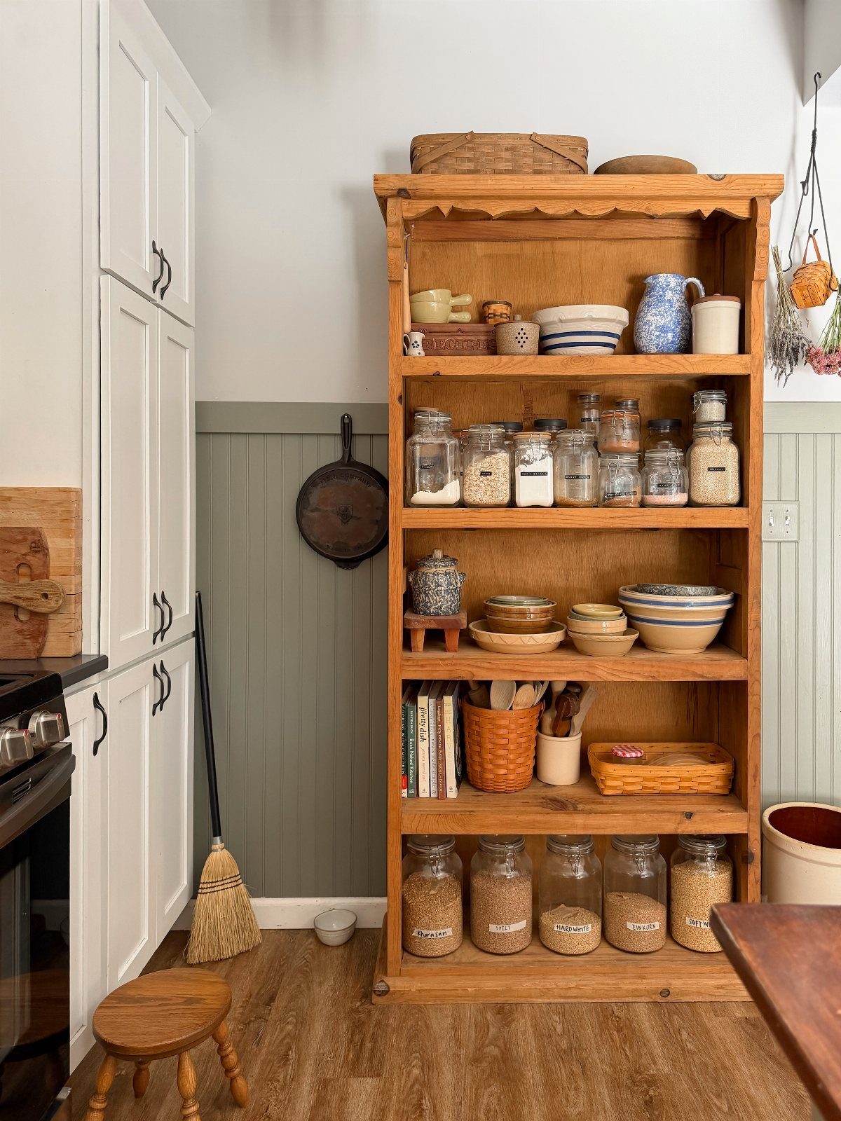Wooden bookshelf repurposed as a kitchen pantry holding glass jars and ceramic bowls.
