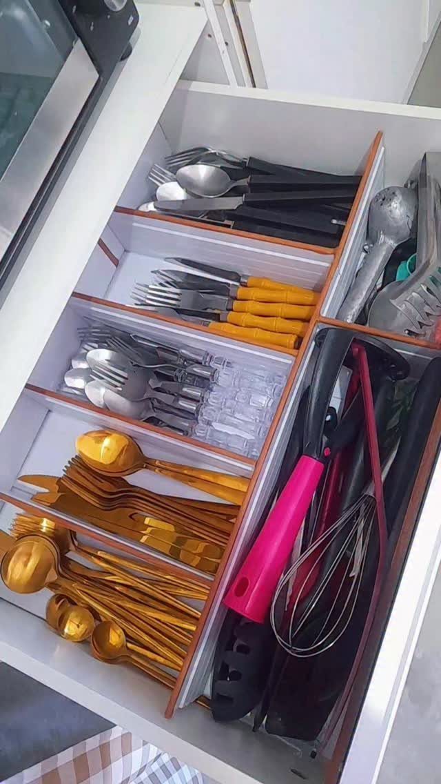 Organized kitchen drawer with wooden dividers holding gold, silver, and colorful cutlery.