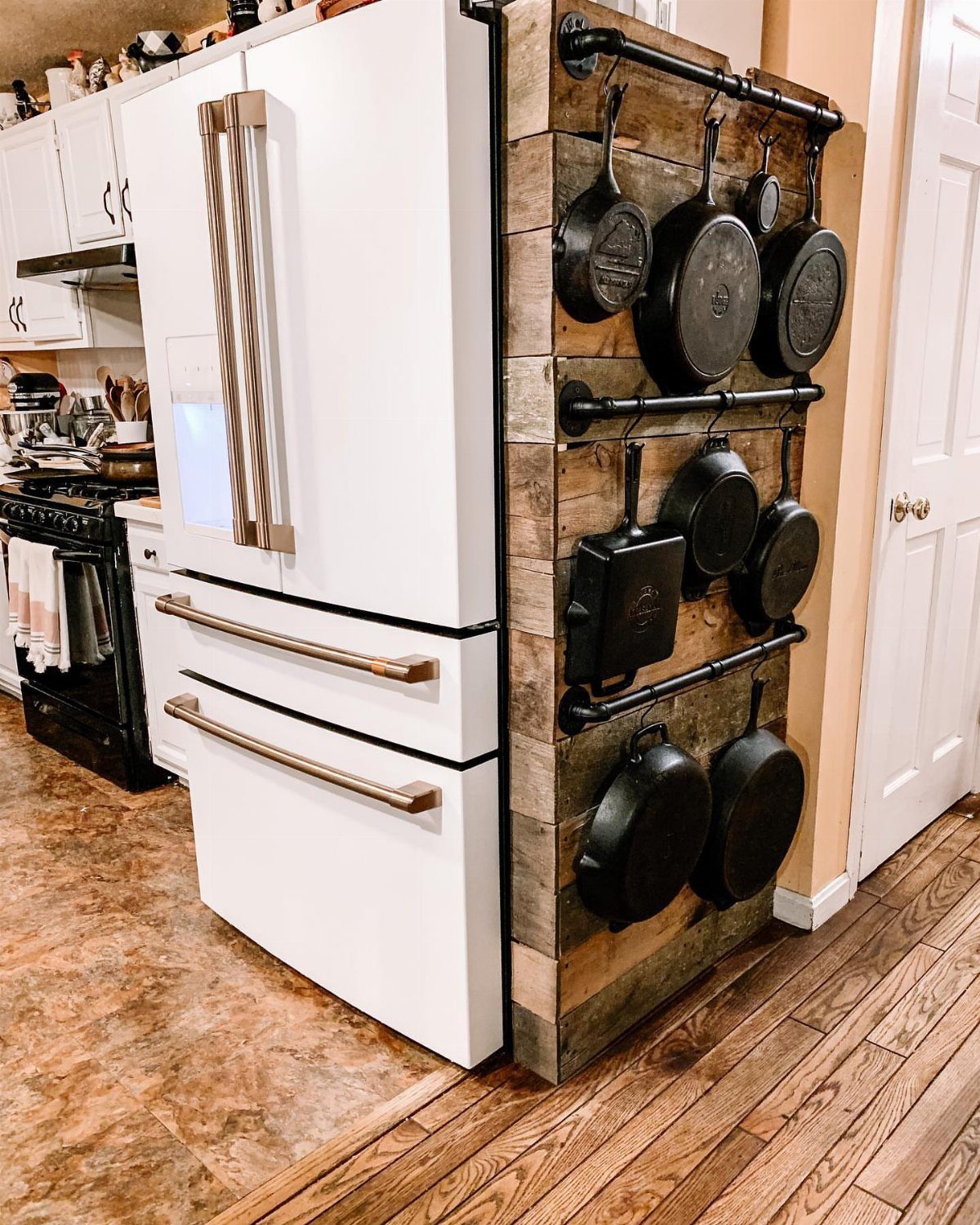 Cast iron pans hanging from black pipe racks on a rustic wooden wall.