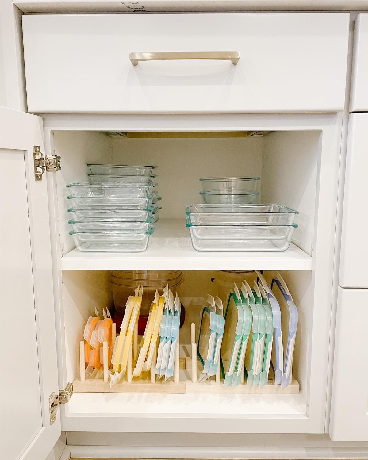 Glass food containers stacked on a shelf with lids stored vertically in an organizer