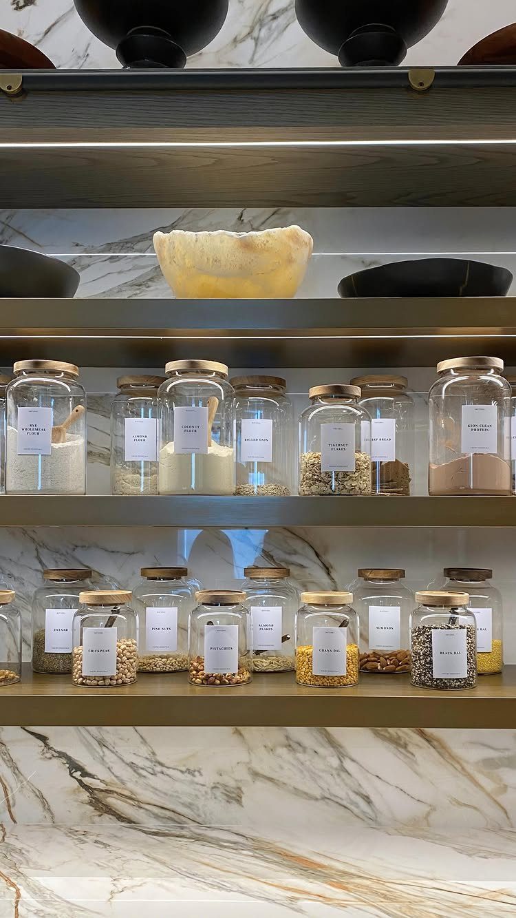 Glass jars with white labels containing grains on metallic kitchen shelves