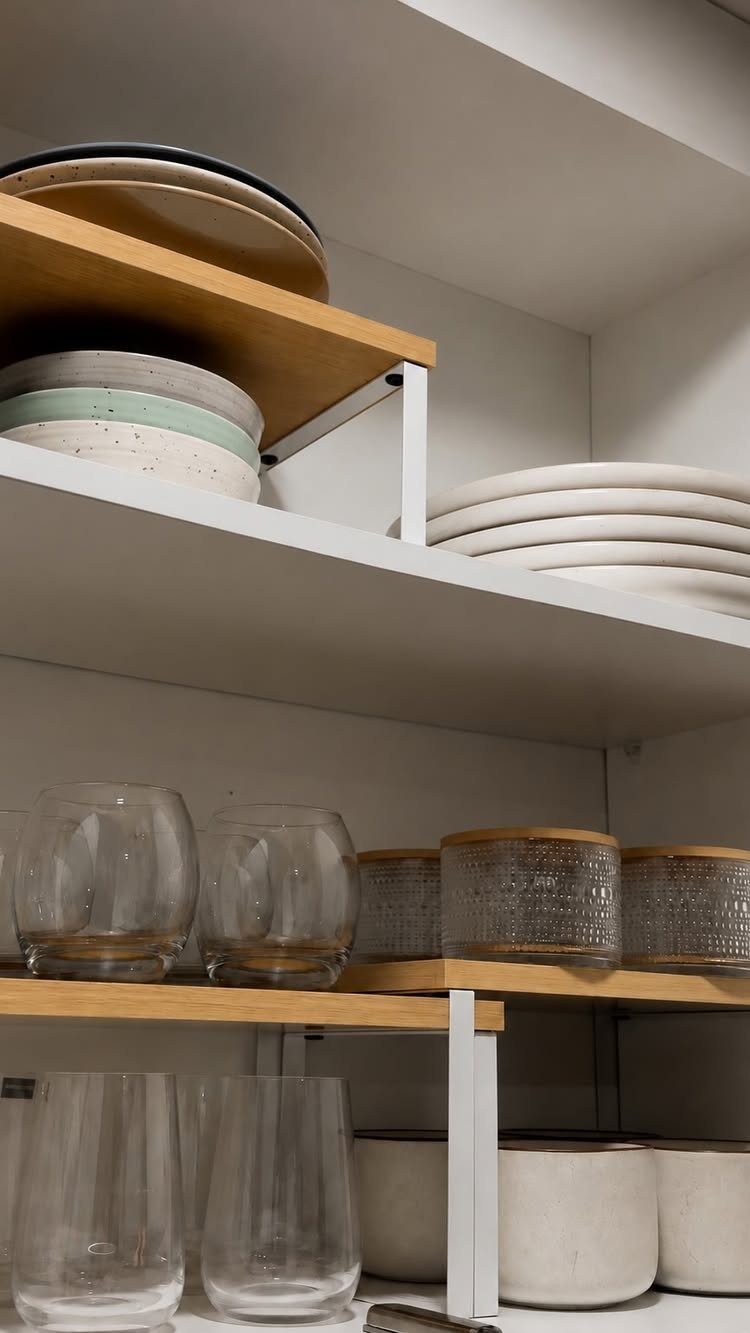 Wooden tiered shelf risers holding plates and glasses inside white kitchen cabinets.