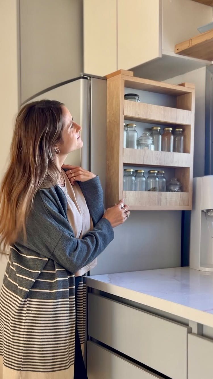 Woman looking at glass jars stored on a wall-mounted wooden kitchen shelf