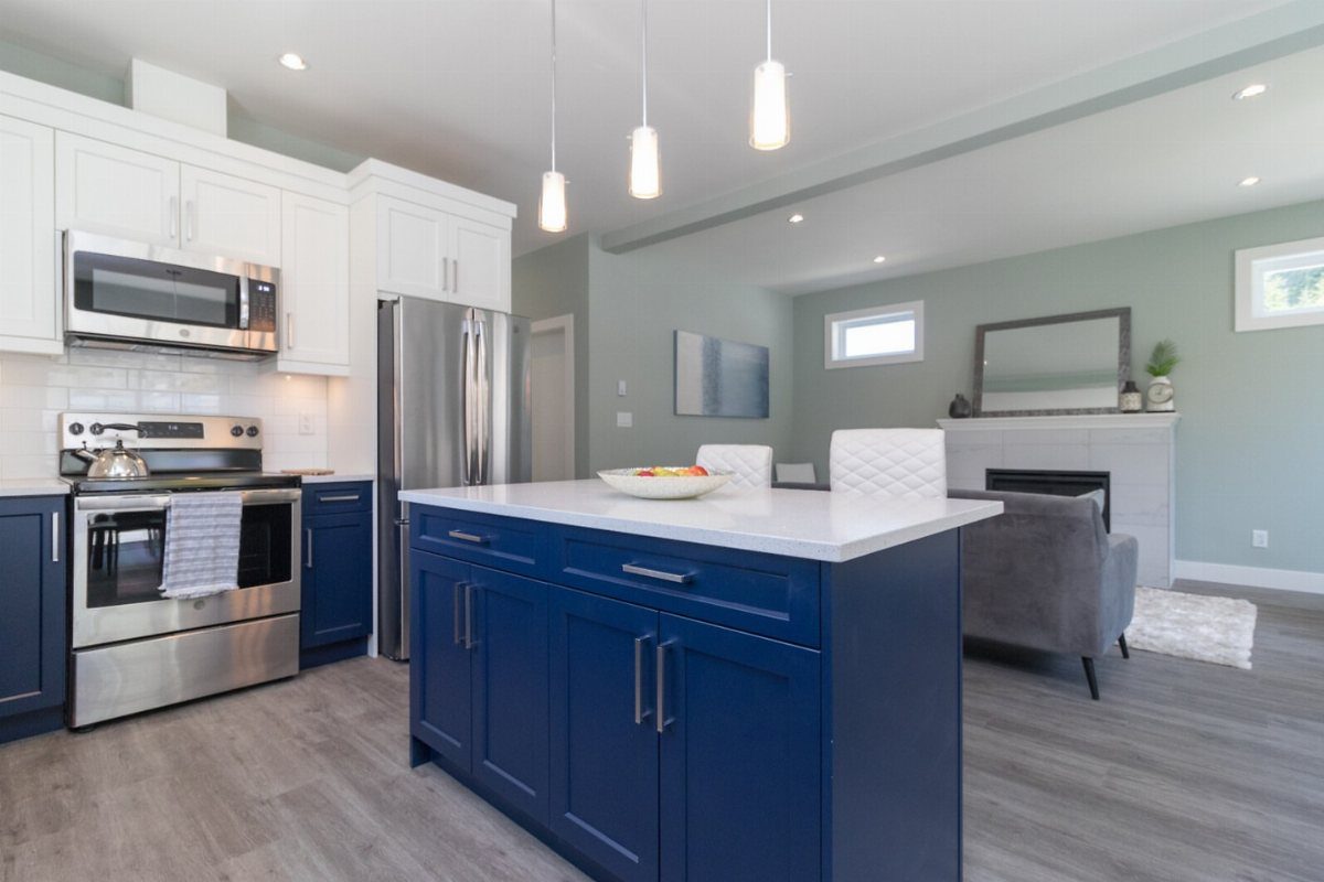 Open concept kitchen with blue island looking toward a grey sofa and fireplace