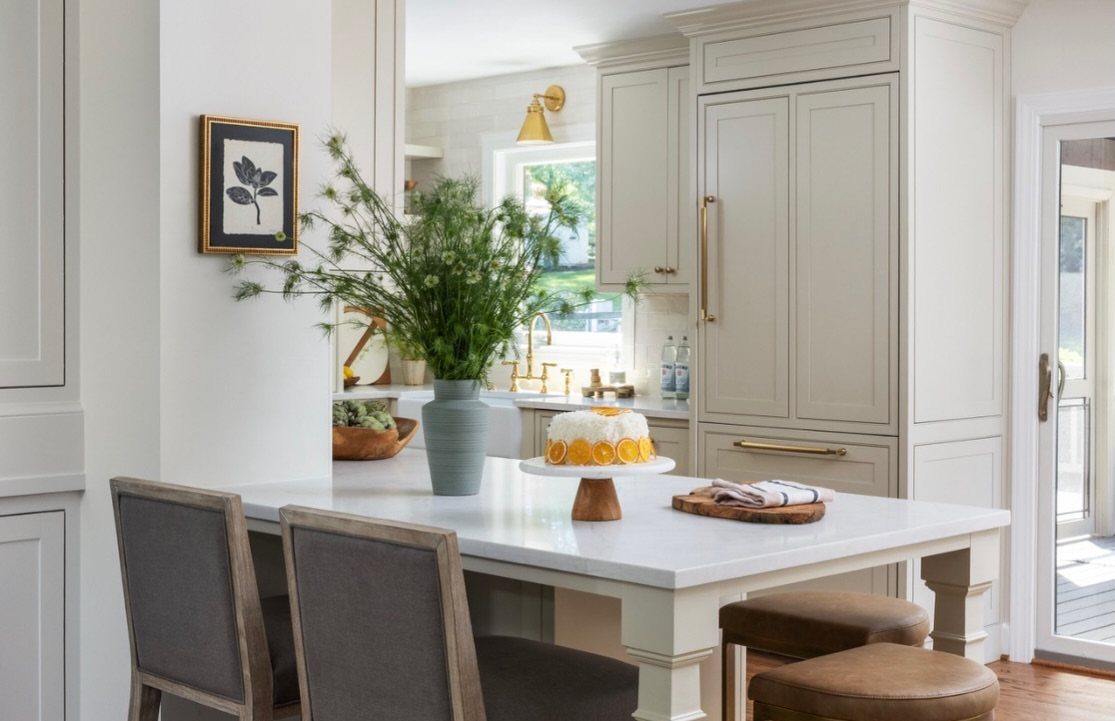 White kitchen island with a cake, grey chairs, and white cabinetry.