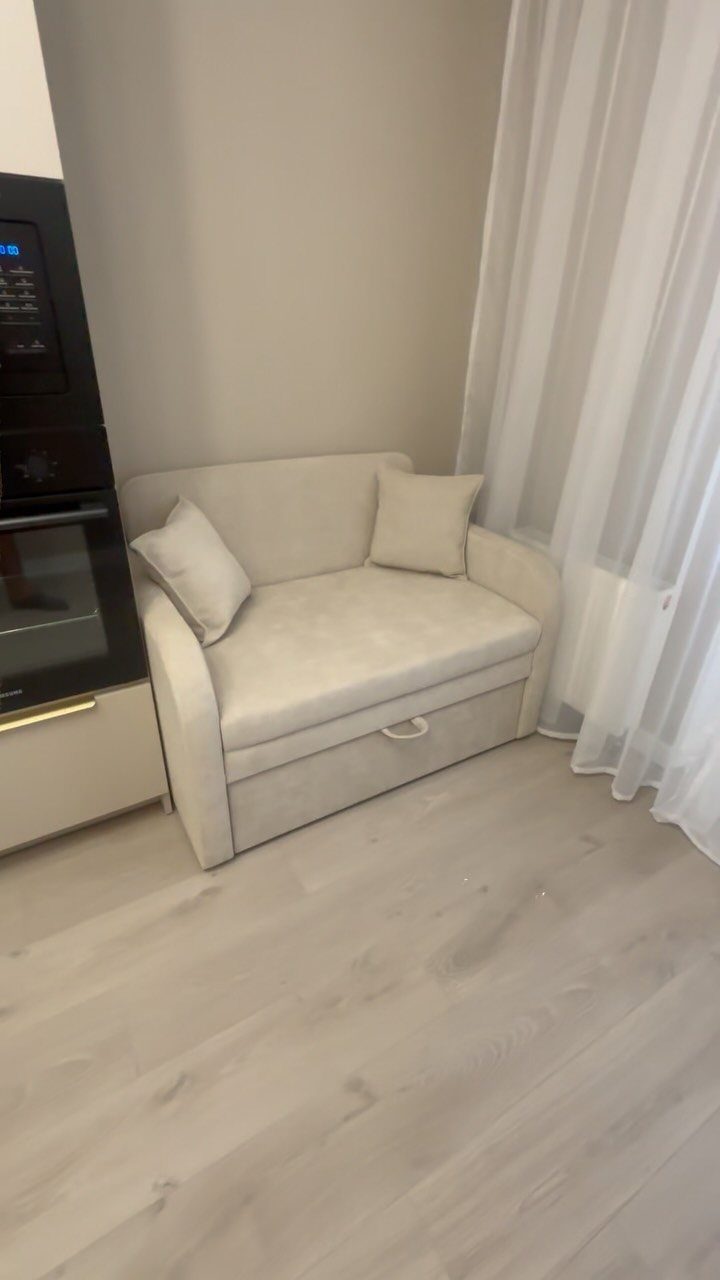 Beige loveseat placed next to a built-in oven in a small open space.