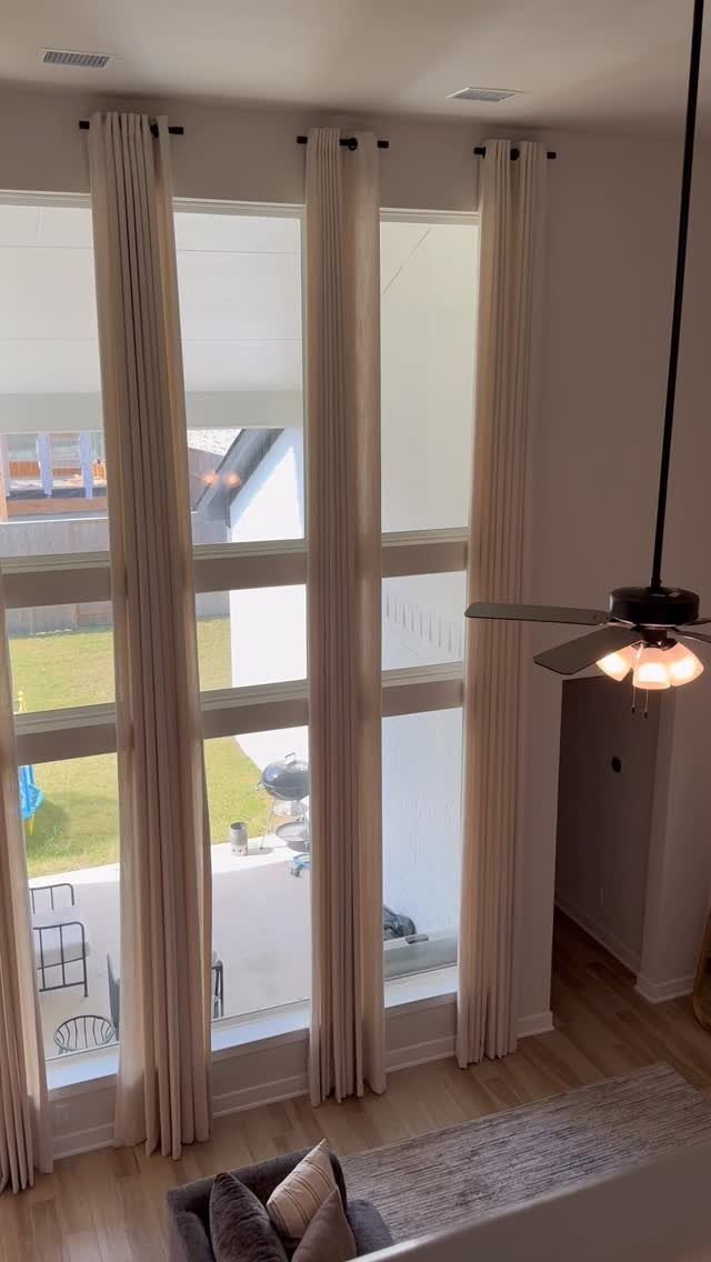 Cream-colored tall curtains hanging from a black rod over large windows