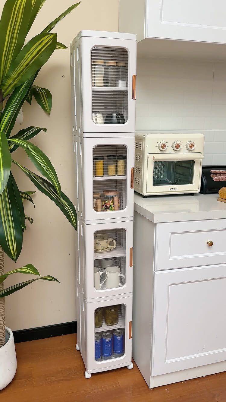 Tall white narrow storage cabinet with glass doors next to a kitchen counter.