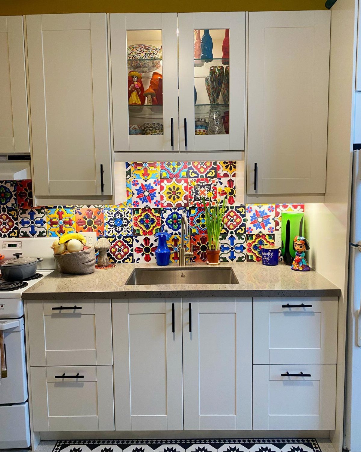Vibrant multicolored patterned tile backsplash in a small white kitchen with grey countertops.