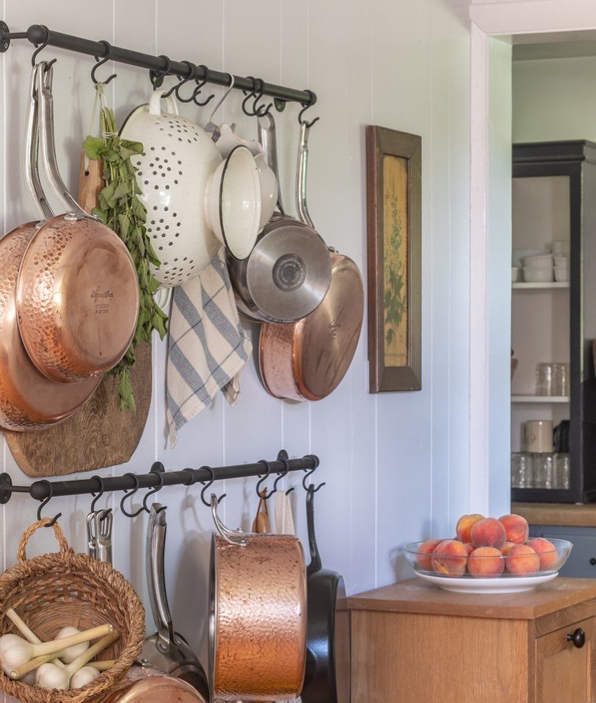 Copper pots and white colanders hanging from black metal rails on white walls.