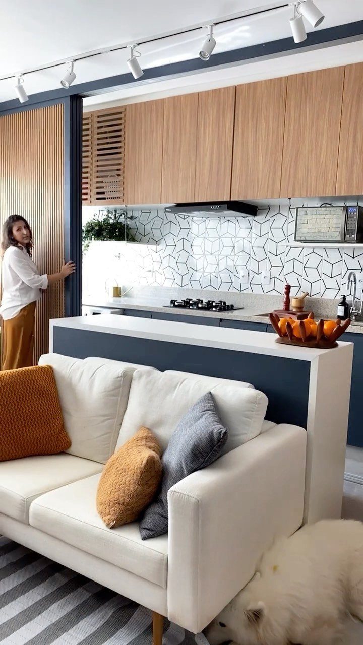 Modern small kitchen with wood cabinets and geometric tiles next to a white sofa.
