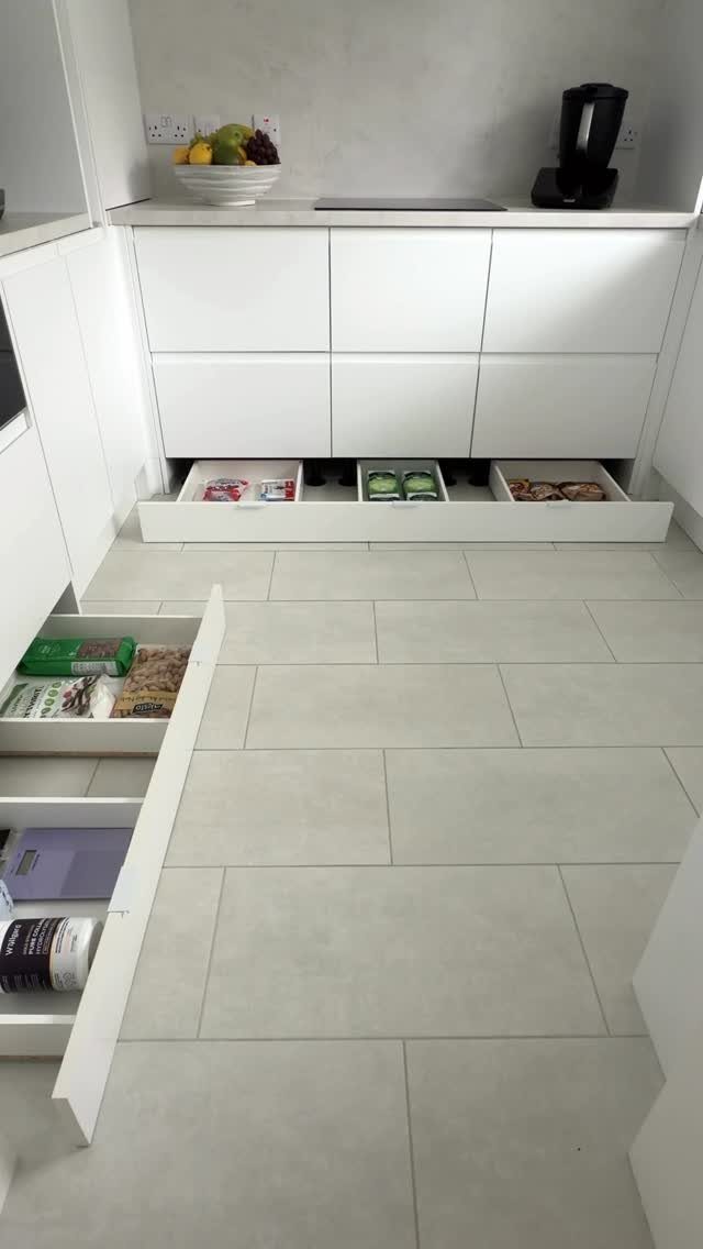 White modern kitchen cabinets with a wide shallow pull-out storage drawer at the base.