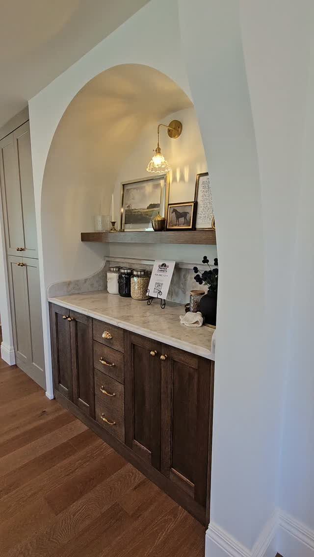 Arched alcove with dark wood cabinets, stone countertop, and a gold wall sconce.