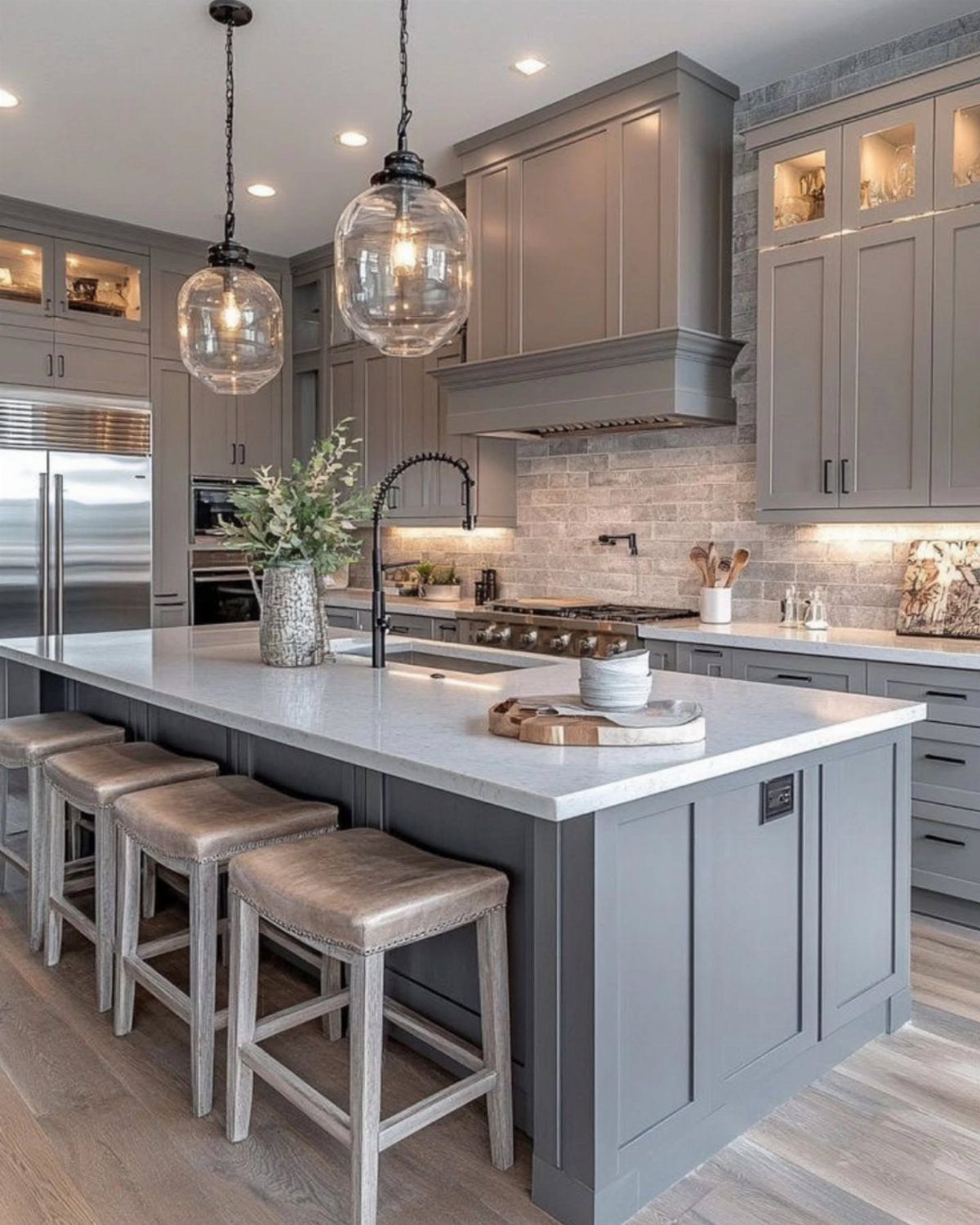 Gray kitchen cabinets with a white marble island and glass pendant lighting.