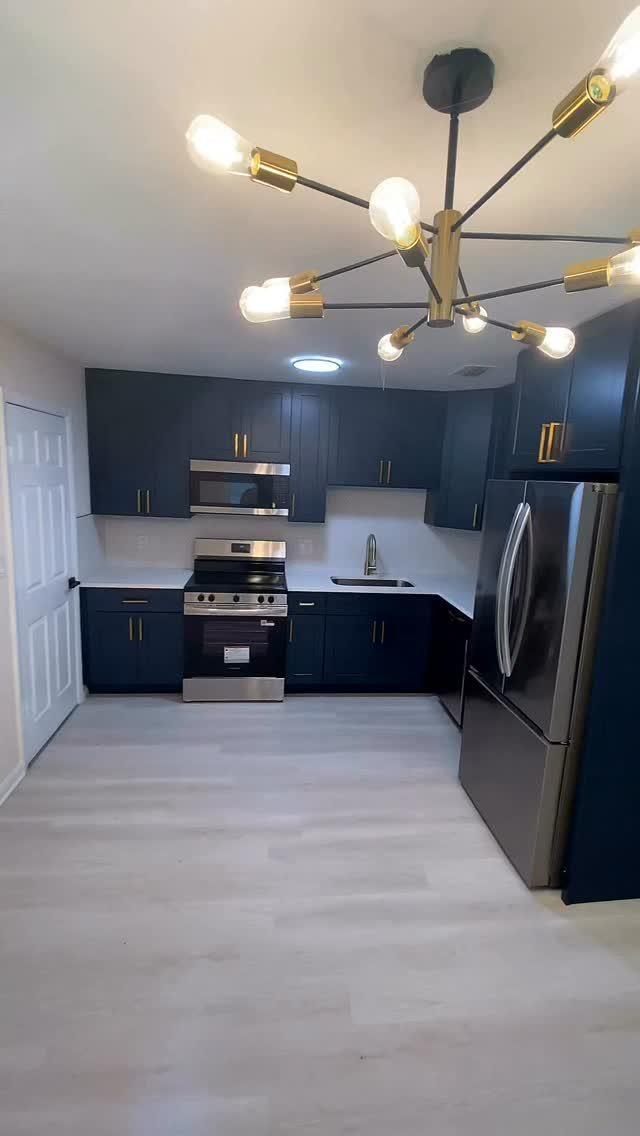 Navy blue kitchen cabinets with gold hardware and stainless steel appliances.
