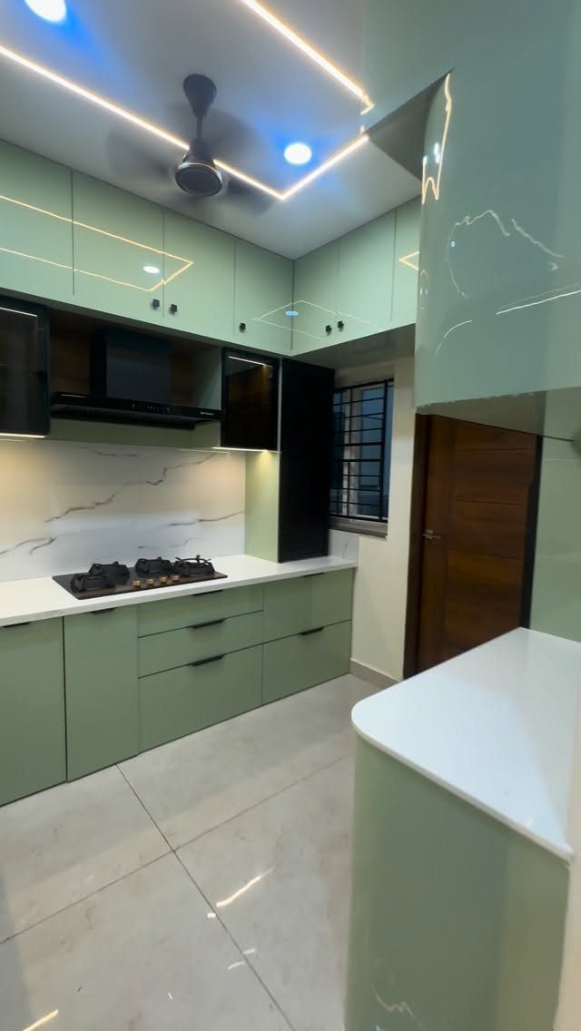 Sage green glossy kitchen cabinets with white countertops and marble backsplash.