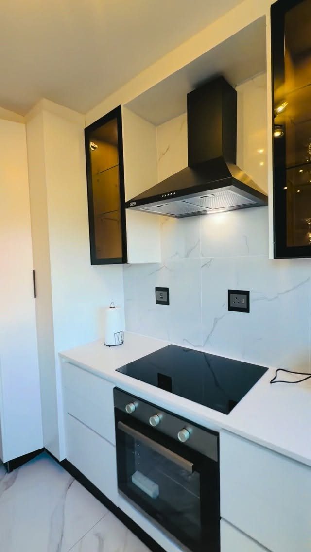 White kitchen cabinets with a marble backsplash and black appliances in a modern design.