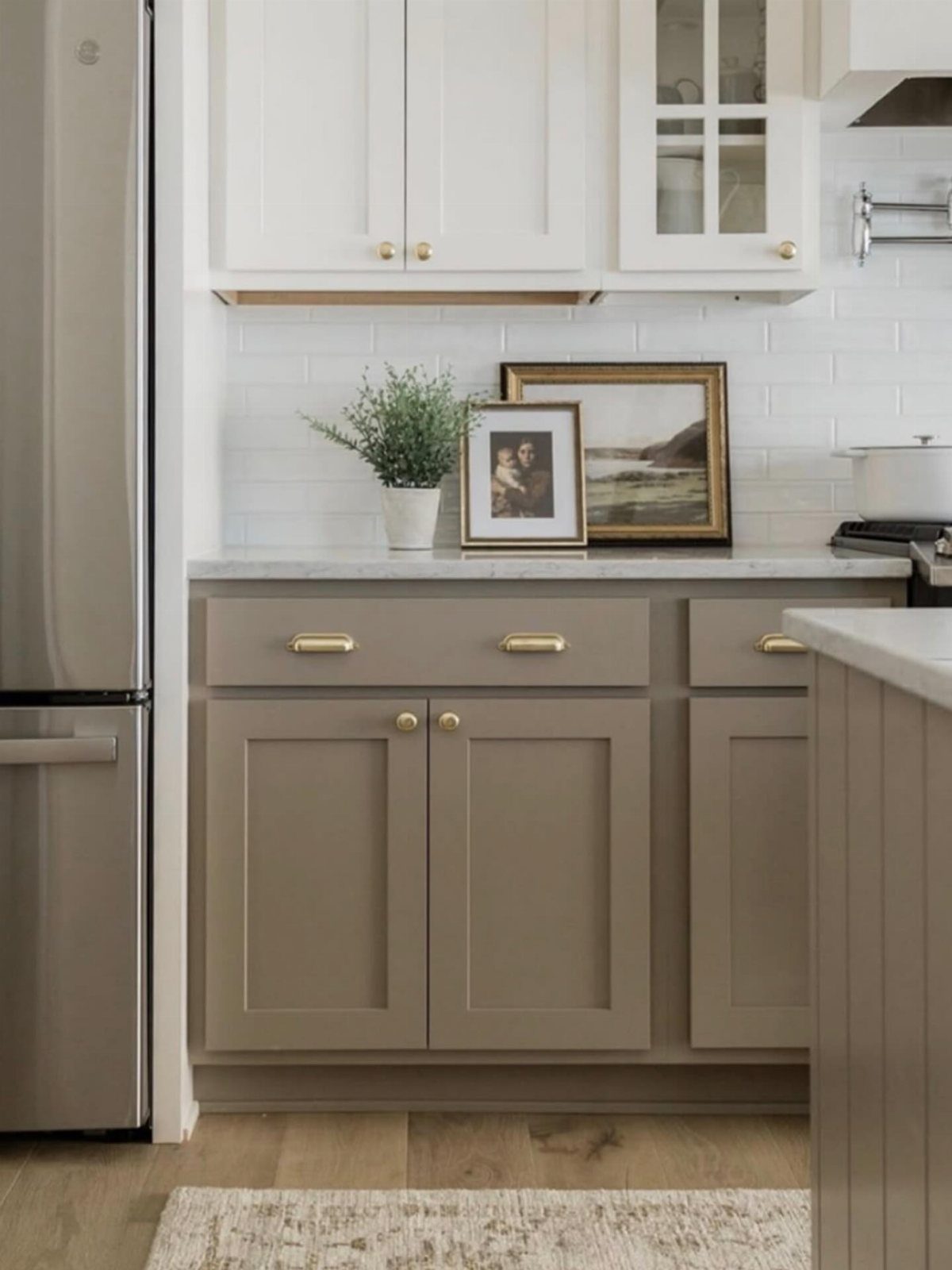 Greige lower cabinets and white upper cabinets in a modern kitchen with gold hardware.