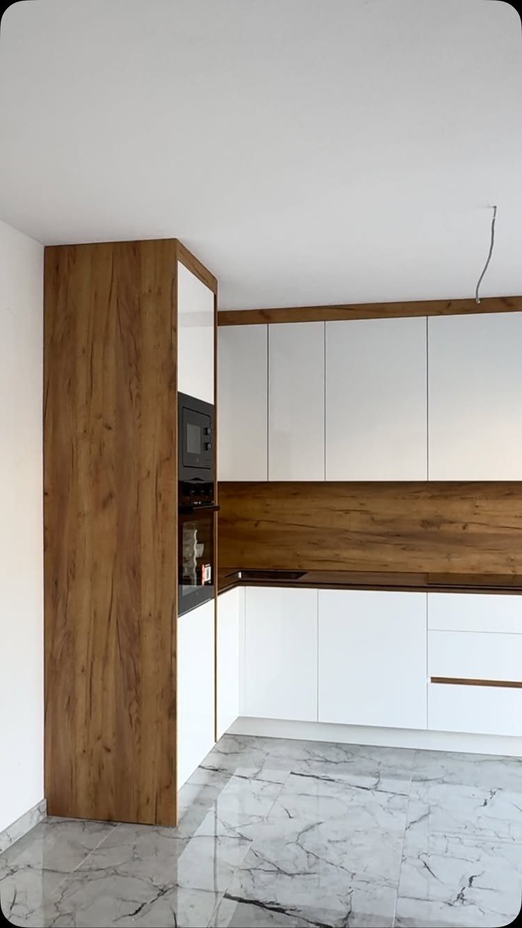 Modern kitchen with white cabinets and natural wood grain accents on marble flooring