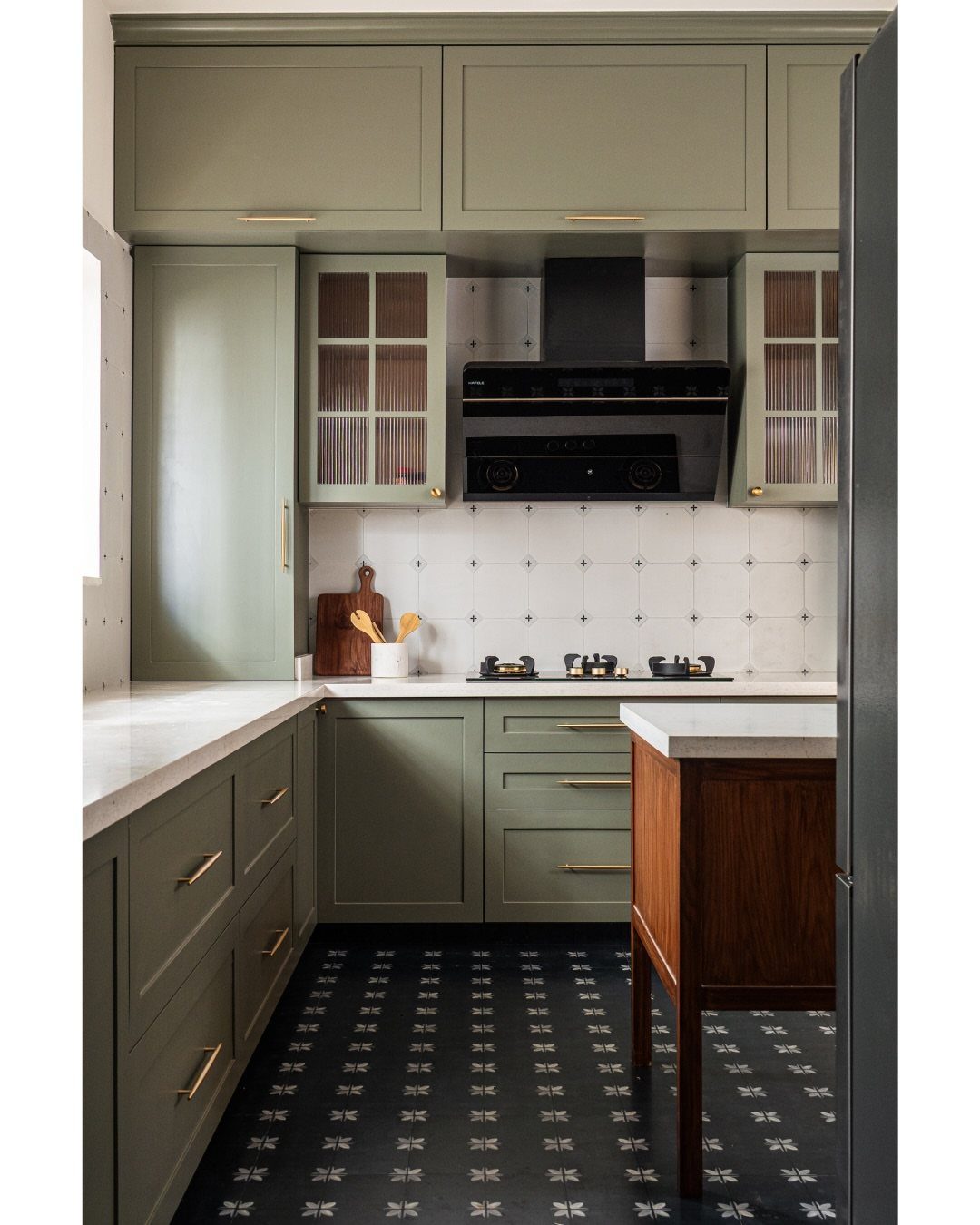 Sage green kitchen cabinets with white countertops and a dark wood island.