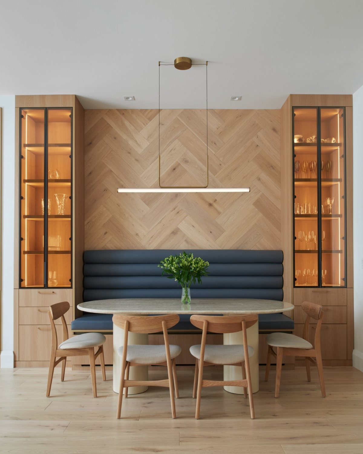 Blue banquette seating and glass-fronted cabinets in a modern light wood dining nook.