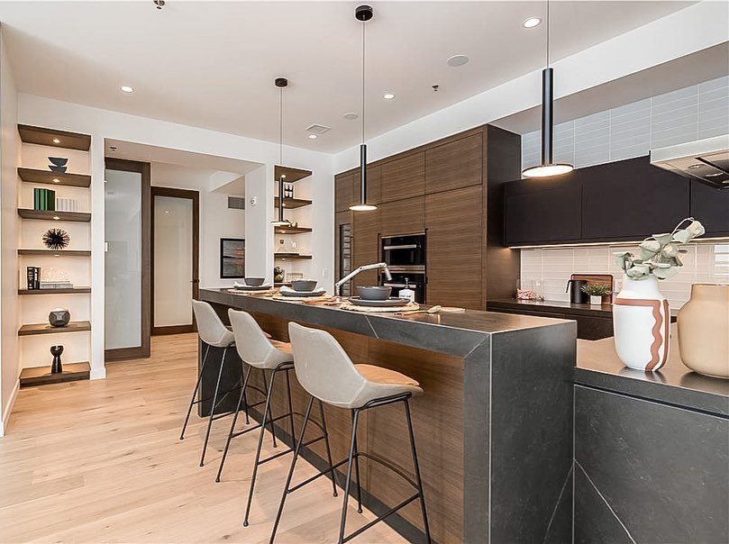 Two level island kitchen with dark grey countertops and white modern bar stools.