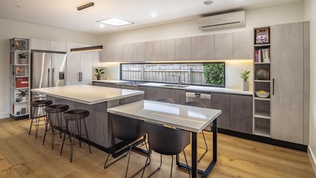 Two-level kitchen island with white countertops, black stools, and grey modern cabinetry.