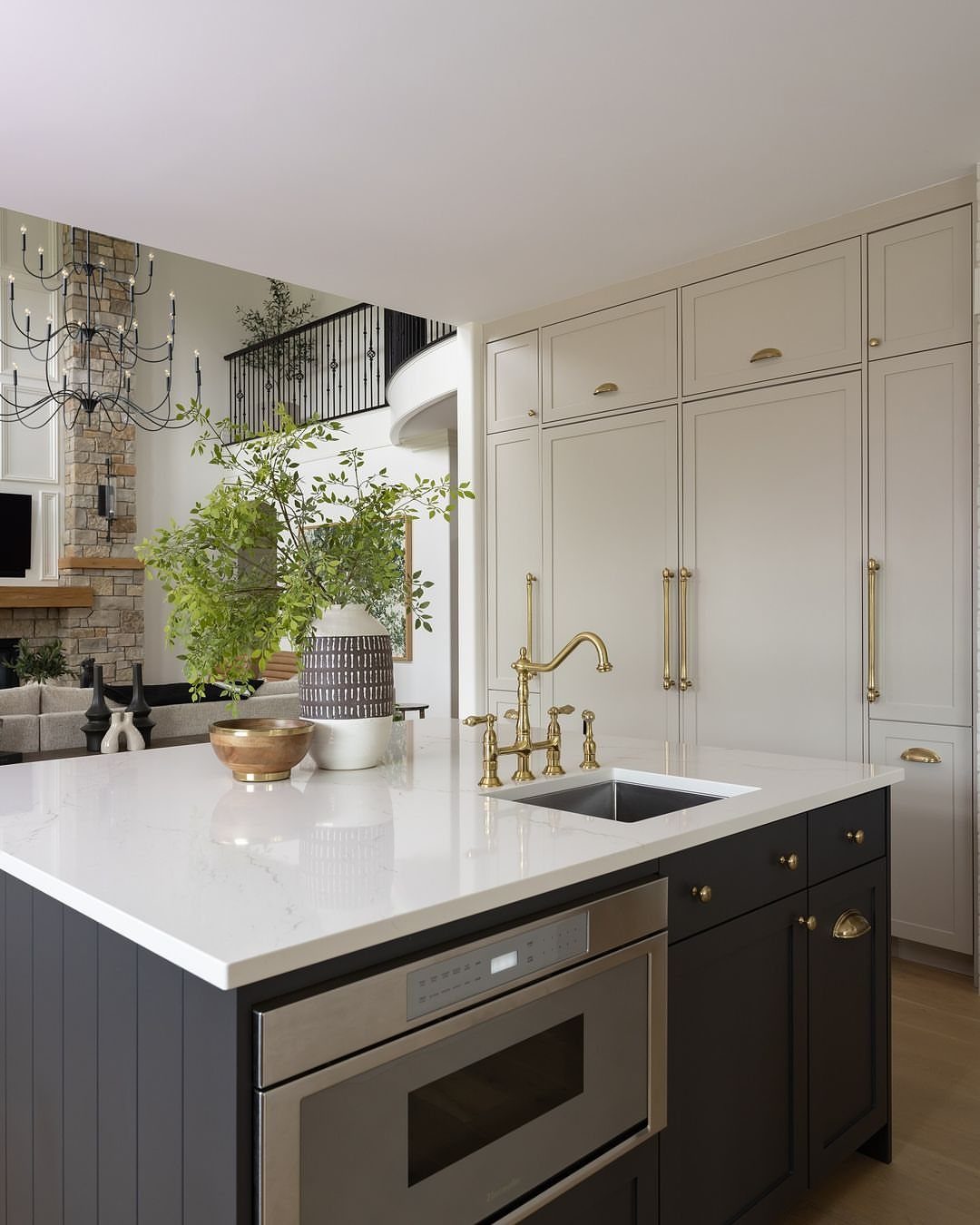 Dark grey kitchen island with brass hardware and white upper cabinets in background