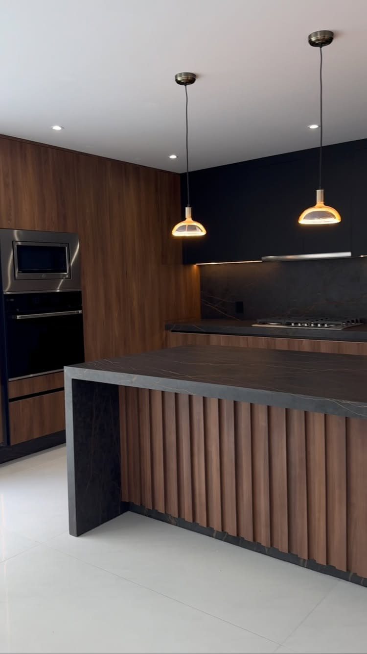 Modern kitchen with dark grey cabinets and warm wood paneling on walls and island.