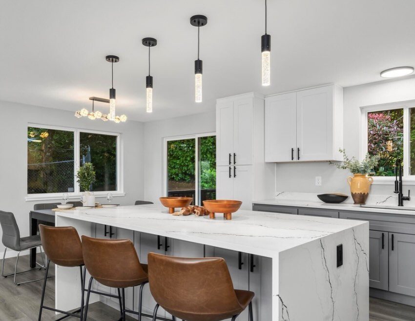 White upper cabinets and gray lower cabinets with white marble countertops and leather stools.