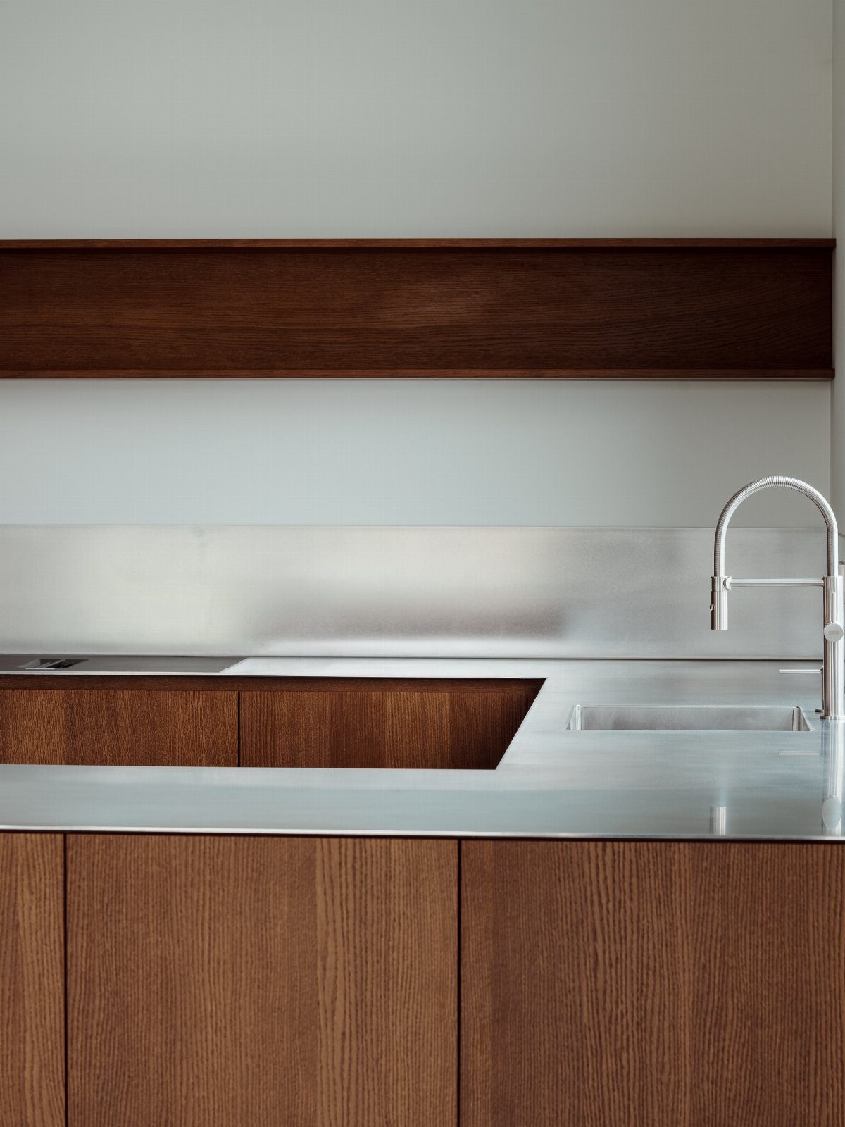Walnut kitchen cabinets and floating shelf with stainless steel countertops and sink.