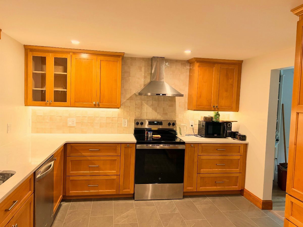 Honey-toned wood kitchen cabinets with white countertops and stainless steel appliances.