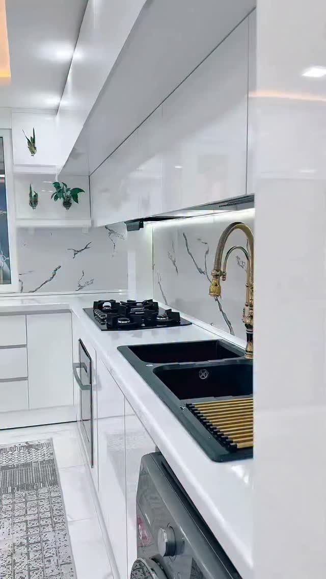 Modern white kitchen with glossy cabinets, marble backsplash, and a gold faucet.