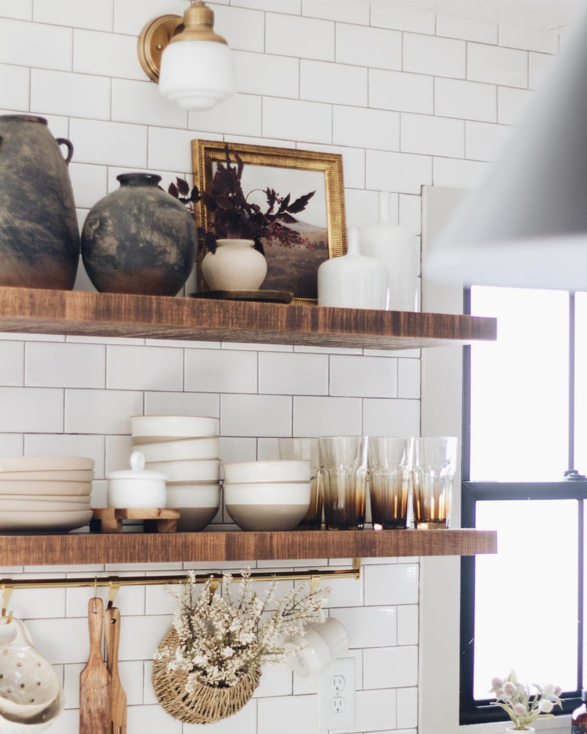 Wooden open shelves with gold accents and white ceramics against white tile walls.
