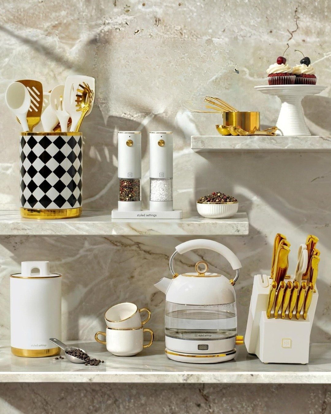 White and gold kitchen accessories arranged on white marble shelving.